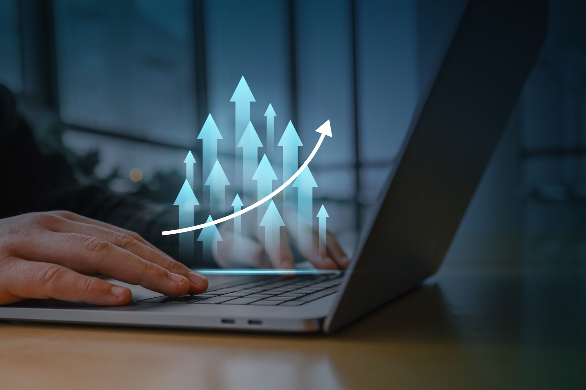 A person working on a laptop with a digital overlay of glowing upward arrows and a rising graph. Concept of business growth, success, financial progress, and digital marketing strategy